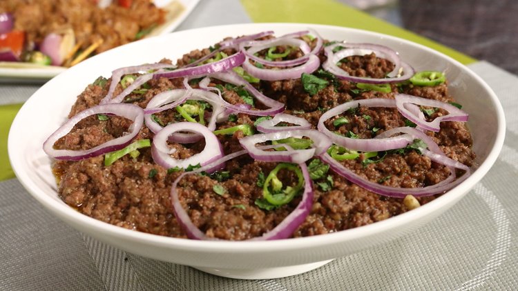 “Hyderabadi-style qeema topped with thinly sliced red onions and green chilies in a white bowl.”