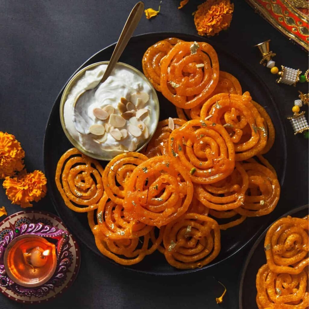 Plated jalebis with a metal spoon – dark background adds contrast, highlighting their saturated orange hue and shine.