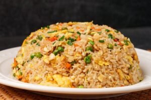 A dome-shaped mound of golden egg fried rice on a white plate, visible grains of rice mixed with peas, carrots, and scrambled egg—classic home-style Chinese fried rice.