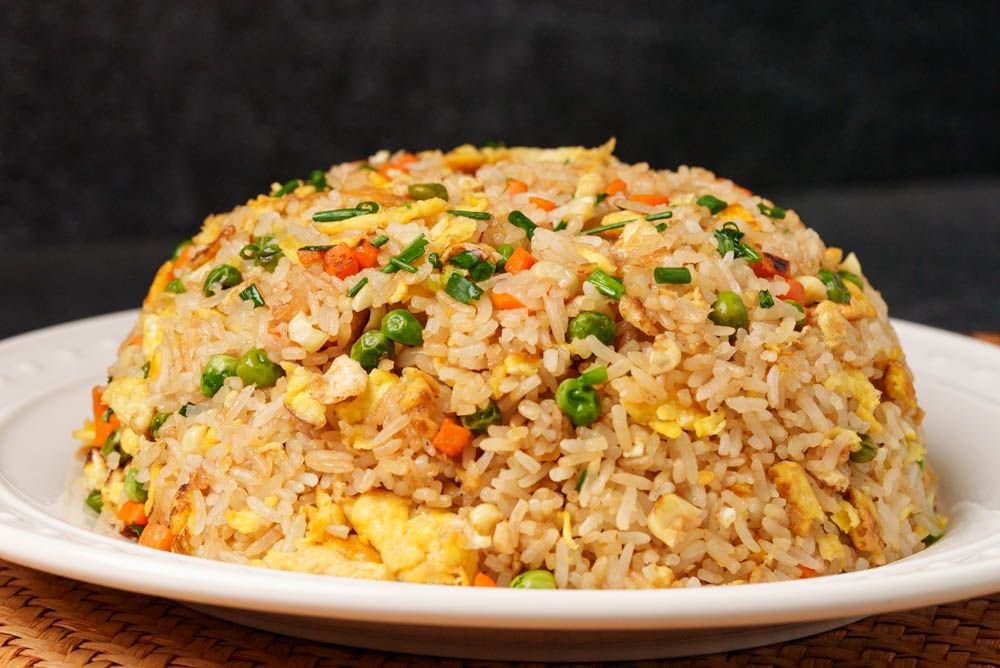 A dome-shaped mound of golden egg fried rice on a white plate, visible grains of rice mixed with peas, carrots, and scrambled egg—classic home-style Chinese fried rice.