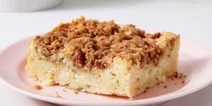 “Slice of zucchini coffee cake on a white plate: tender, moist yellow-green cake flecked with green zucchini strands, topped with a golden-brown cinnamon–brown sugar streusel layer.”