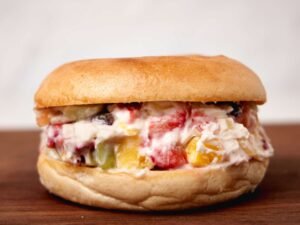 “Toasted bagel halves generously smeared with sweetened cream cheese and mixed chopped fruit—including pineapple, strawberries, melon and kiwi—tinged with powdered sugar, creating a colorful, bite‑sized fruit pizza on a bagel.”