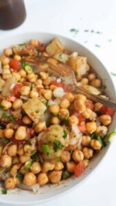 Street‑style black chickpea (kala chana) chaat served in a paper cone, garnished with chopped onions, tomatoes, green chutney, tamarind sauce, and fresh coriander.