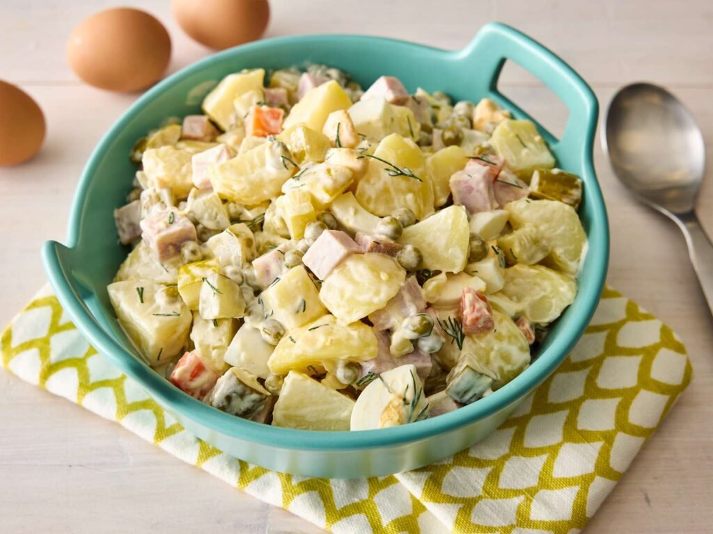A turquoise bowl of diced potatoes, carrots, peas, eggs, ham, pickles, and mayo—captured in bright light that highlights the salad’s chunky, creamy texture