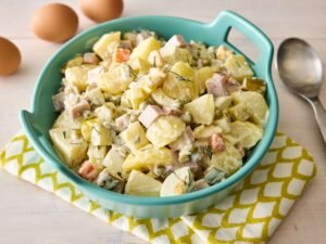 A turquoise bowl of diced potatoes, carrots, peas, eggs, ham, pickles, and mayo—captured in bright light that highlights the salad’s chunky, creamy texture