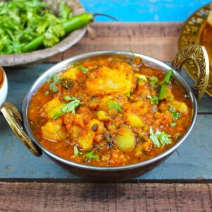 Aloo ki sabzi in a stainless steel dish with sauce-coated potato pieces, sprinkled with coriander