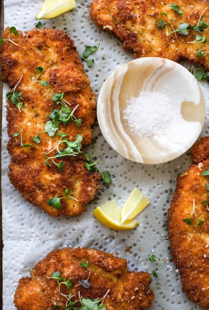 Flat, lightly battered cutlets on a plate, garnished with chopped parsley and accompanied by a dipping sauce (likely mayo‑based).