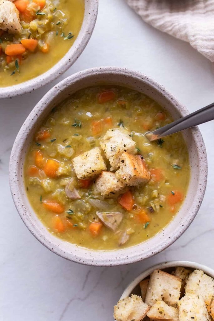 Two rustic bowls of split pea soup with hearty chunks and crisp croutons, photographed from overhead on a white surface.