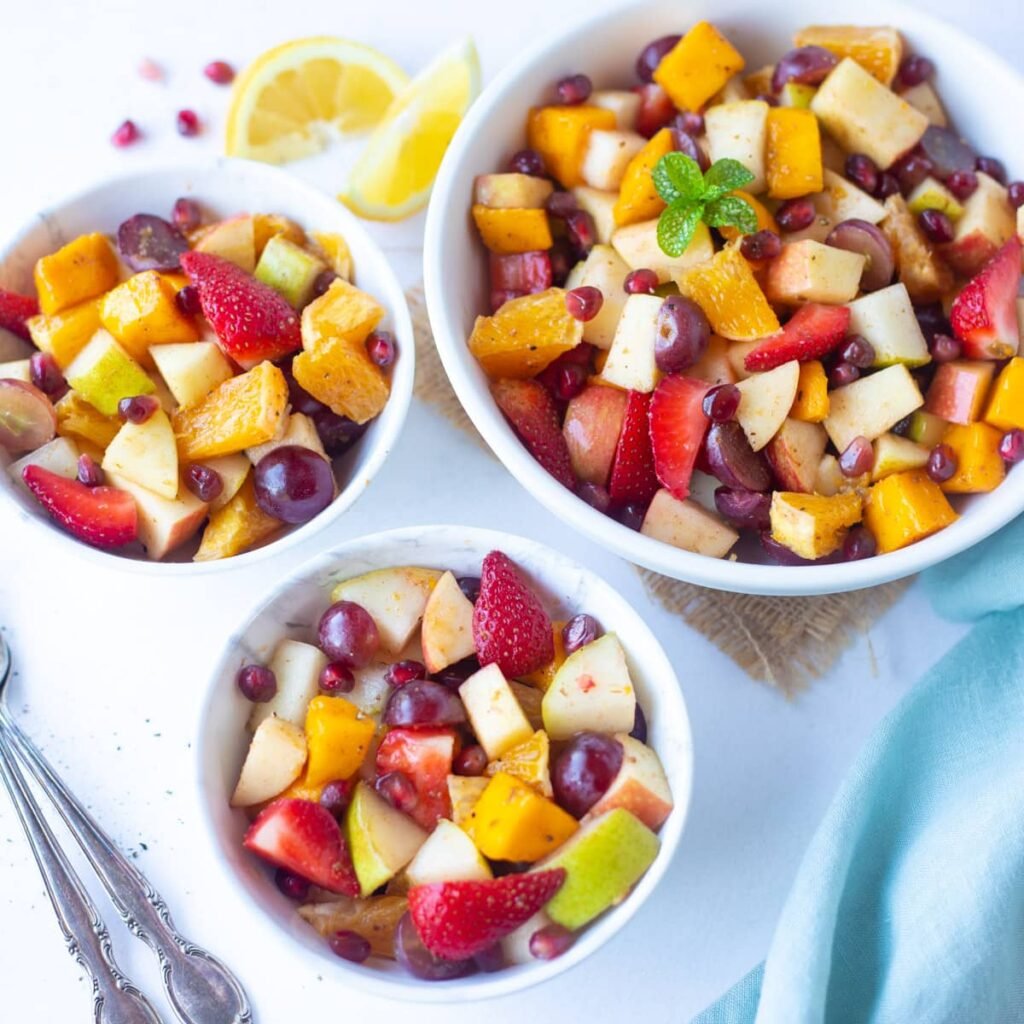 “Colorful mixed fruit chaat in a bowl with apple, banana, grapes, pomegranate, garnished with mint.”