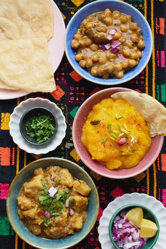 Traditional breakfast spread featuring bright halwa, crispy puris, chickpea curry, and green chutney.