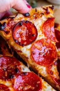 “Slice of homemade pepperoni pizza being lifted, with gooey cheese stretching from the slice.”