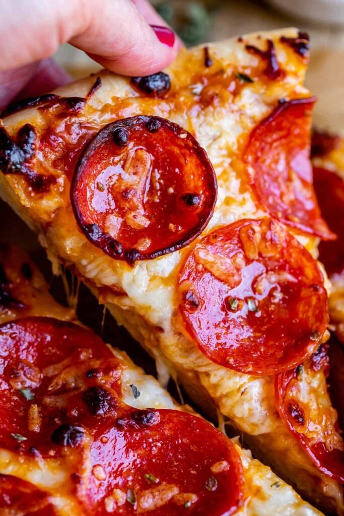 “Slice of homemade pepperoni pizza being lifted, with gooey cheese stretching from the slice.”