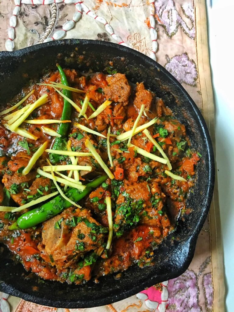 Black karahi pan filled with spicy mutton karahi—chunks of meat in thick red gravy, garnished with julienned ginger and green chilies.”