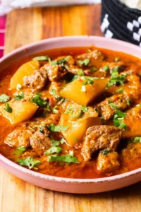 showing tender meat chunks and potato pieces, garnished with chopped cilantro and served with a spoon.