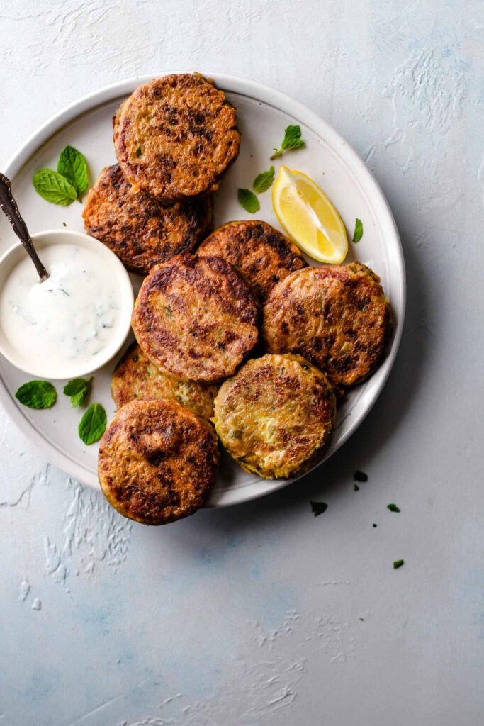 accompanied by a bowl of raita, lemon wedge, and a garnish of fresh mint leaves—crispy exterior, soft center