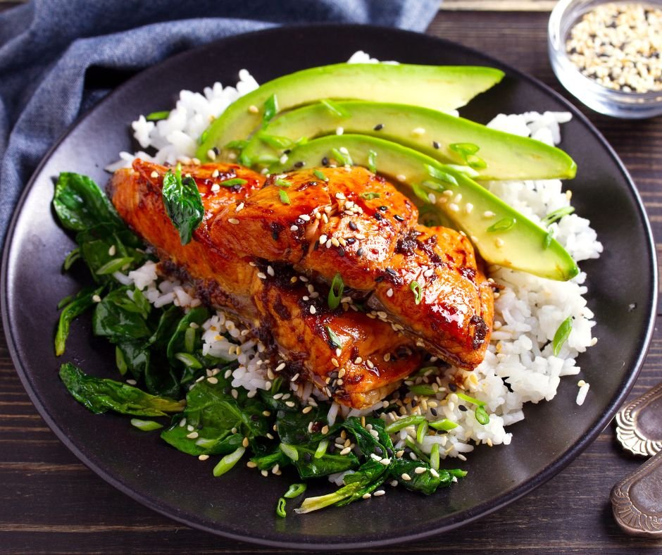 A rice bowl topped with bourbon-baked salmon slathered in sauce, with rice and garnishes including sliced cucumber arranged artfully.