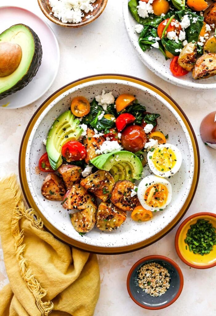 Overhead view of a savory breakfast bowl featuring roasted sweet potato cubes, black beans, cooked chorizo or ground sausage, avocado slices, and a soft-cooked egg with a slightly runny yolk, all arranged artfully in a ceramic bowl.