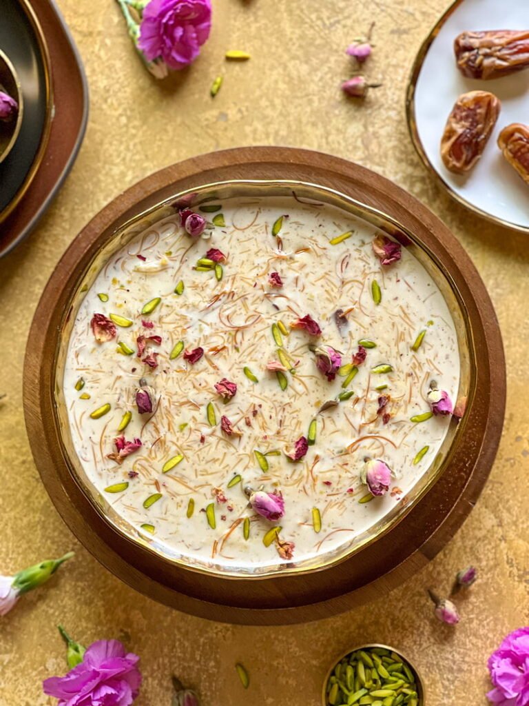 A top-down shot of a rustic bowl filled with creamy Sheer Khurma—milky vermicelli studded generously with chopped nuts and raisins—presented on a wooden surface.