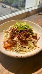 A bowl of Sichuan-style spicy chicken noodles—noodles tossed in richly colored chili oil, topped with tender shredded chicken and fresh green onion.