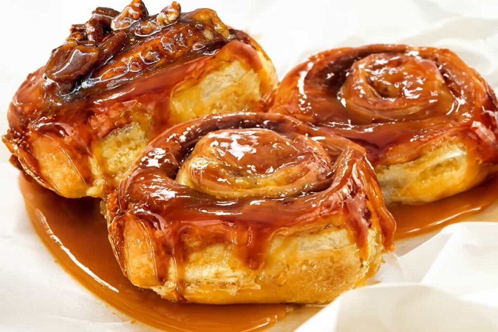 “Close-up of a sticky bun topped with glossy caramel glaze and chopped pecans.”