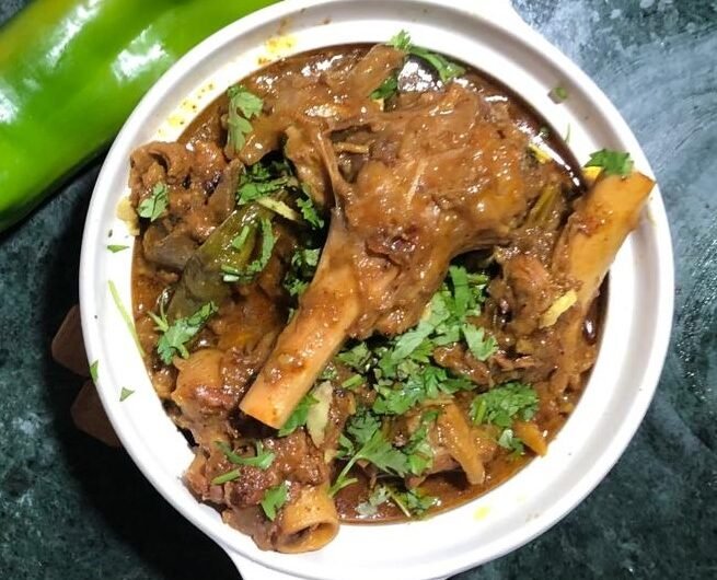 White ceramic bowl containing mutton nihari topped with fresh cilantro and julienned ginger.”