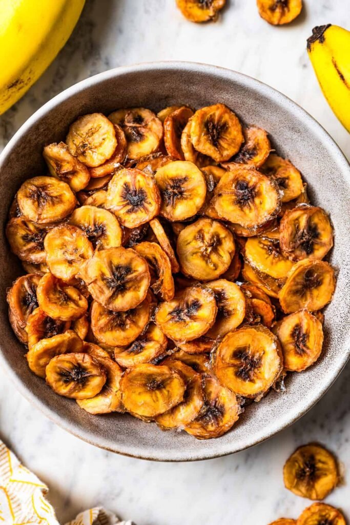 Close-up of round banana chip slices filling a shallow dish, each chip showing golden edges and a slightly caramelized center.