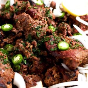 Close-up of richly marinated meat pieces coated in spices, garnished with sliced green chilies—emphasizing the vibrant color and aromatic texture.