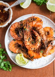 Spicy Cajun tiger prawns in a glossy garlic–lime butter sauce, arranged in a bowl with lime wedges and fresh greens—juicy, vibrant, and ready to serve 