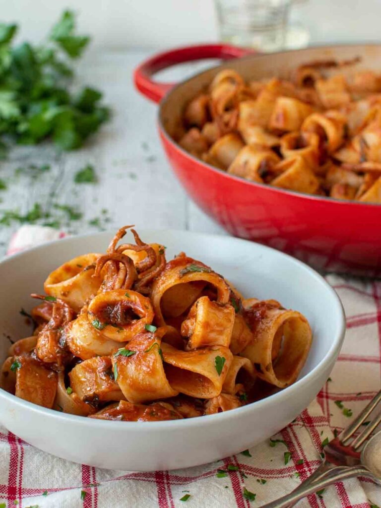 “Calamarata pasta rings with calamari in a garlic‑tomato sauce served in a bowl.”