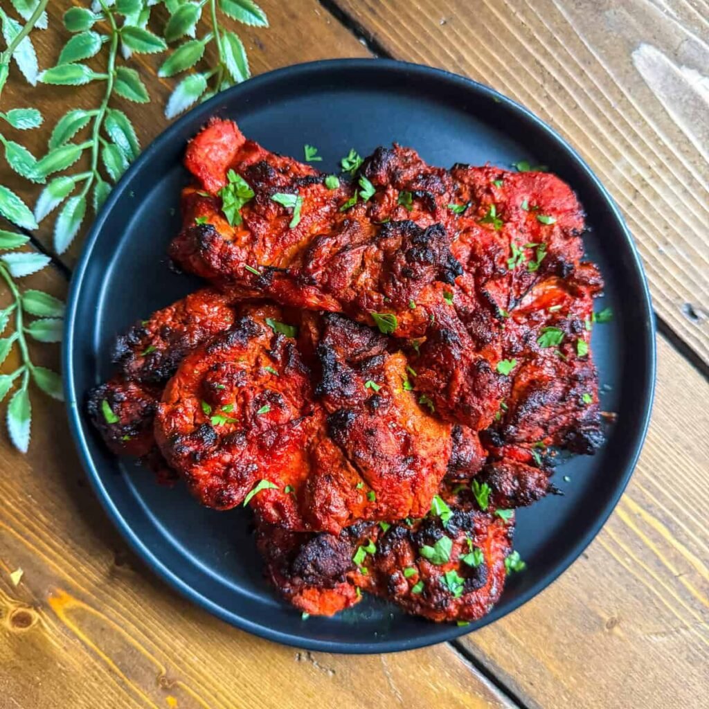 Chicken tikka skewers grilled to perfection and served with green chutney, onions, and lemon wedges on a rustic platter.