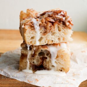 “Two thick squares of cinnamon‑sugar focaccia, stacked and drizzled with vanilla icing, showing gooey layers and fluffy texture.”