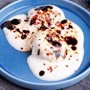 The alt text could be: "Three dahi baray in yogurt with tamarind sauce and chili flakes on blue plate.
