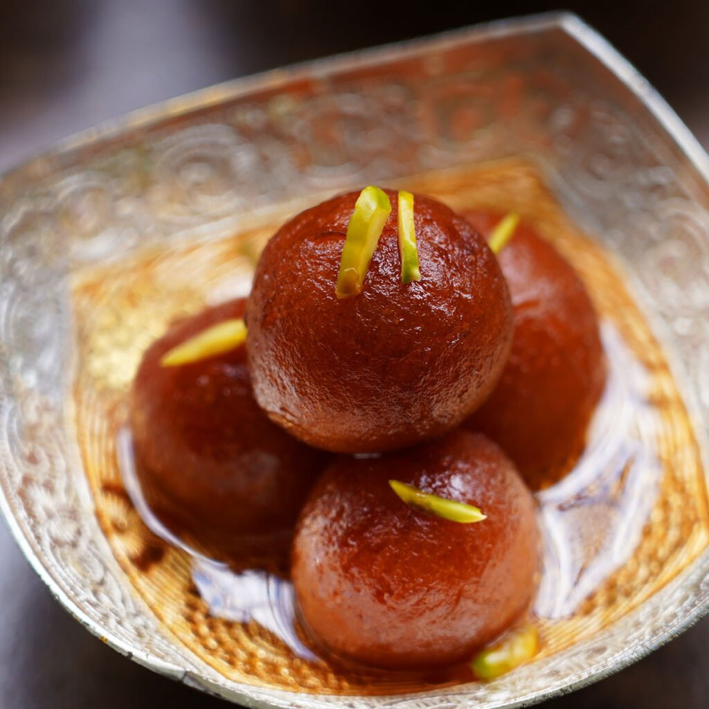 Three juicy gulab jamun balls in syrup, garnished with chopped pistachios.”