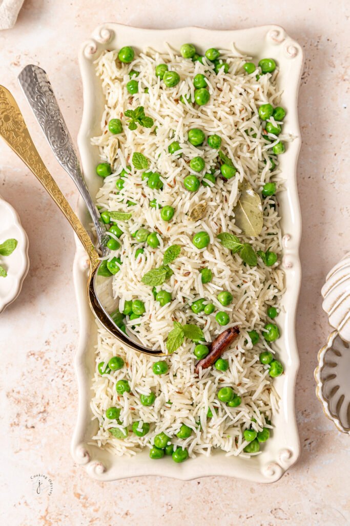 Tray of green pea pulao with fresh mint leaves sprinkled on top, showing grains coated in subtle spices—light and fragrant.