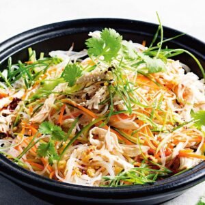 Cold chicken noodle salad in a bowl with colorful vegetables, sesame seeds, and chopsticks on the side.